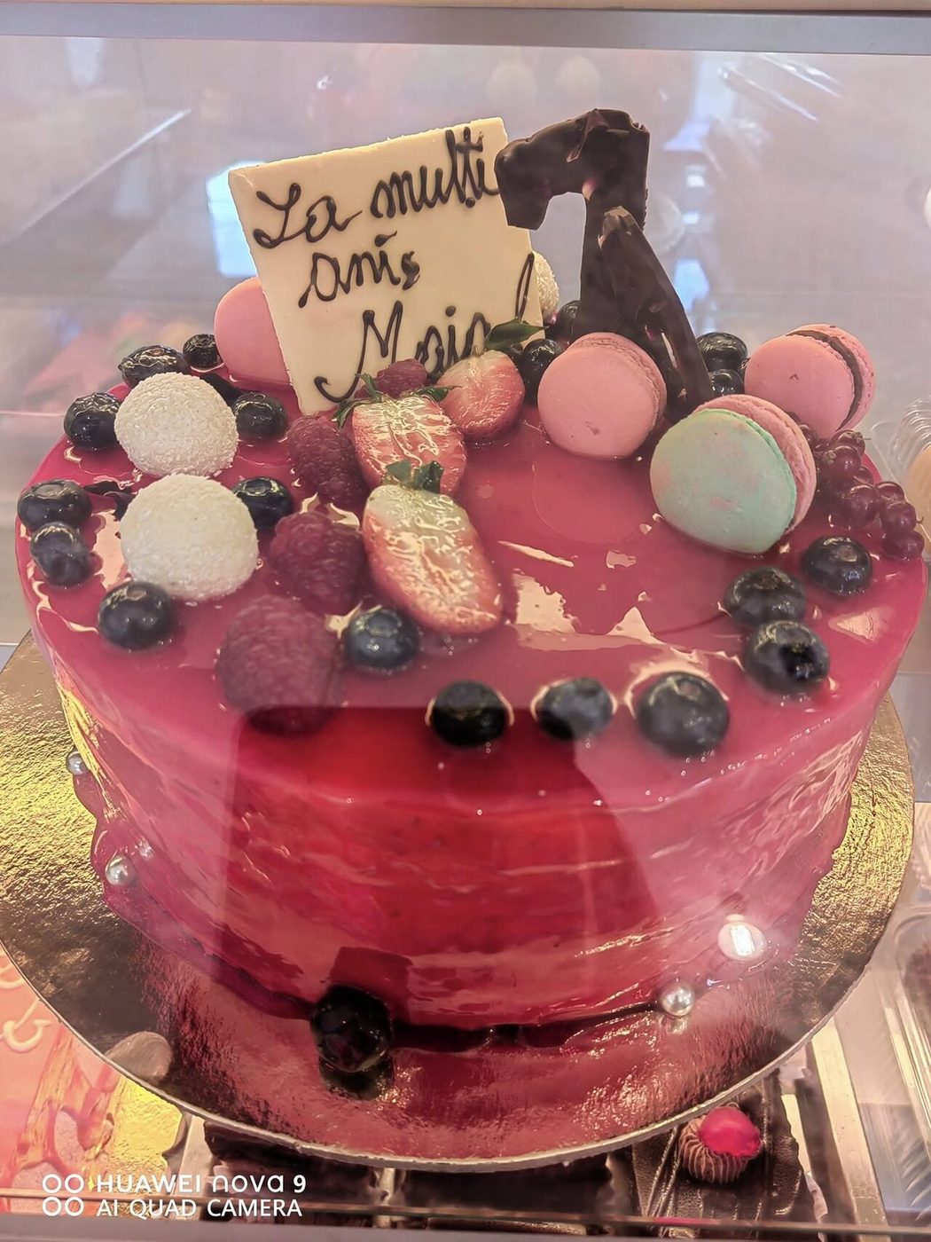 Tort cu glazură roșie de fructe, macarons și fructe de pădure, în vitrină