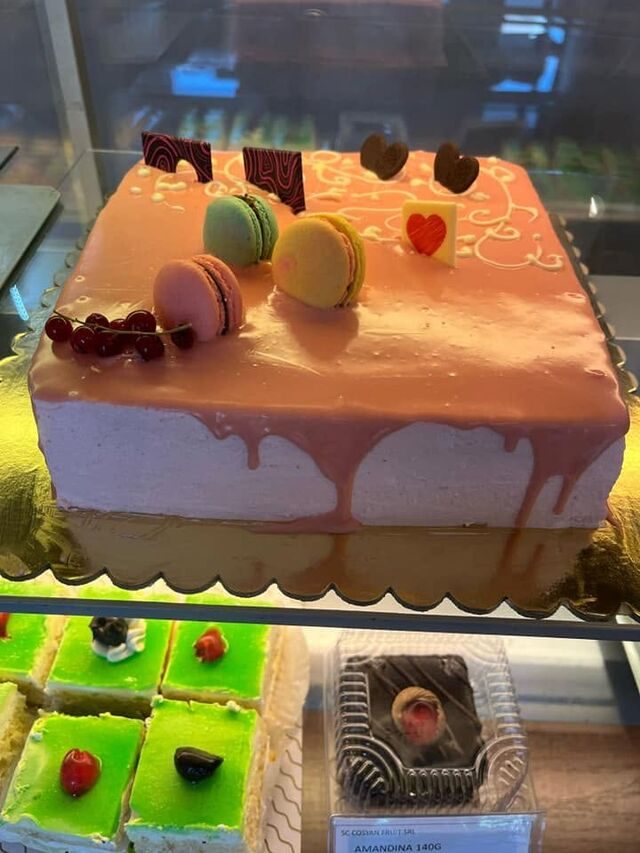 Tort dreptunghiular cu glazură roz, macarons și coacăze, în vitrina patiseriei