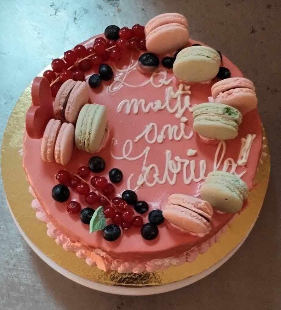 Tort roz decorat cu macarons, coacăze roșii și afine, cu mesaj de aniversare
